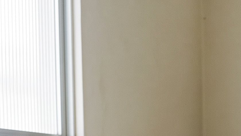 Homem ajoelhado de olhos fechados e mãos postas, com uma Bíblia aberta no sofá da sala.