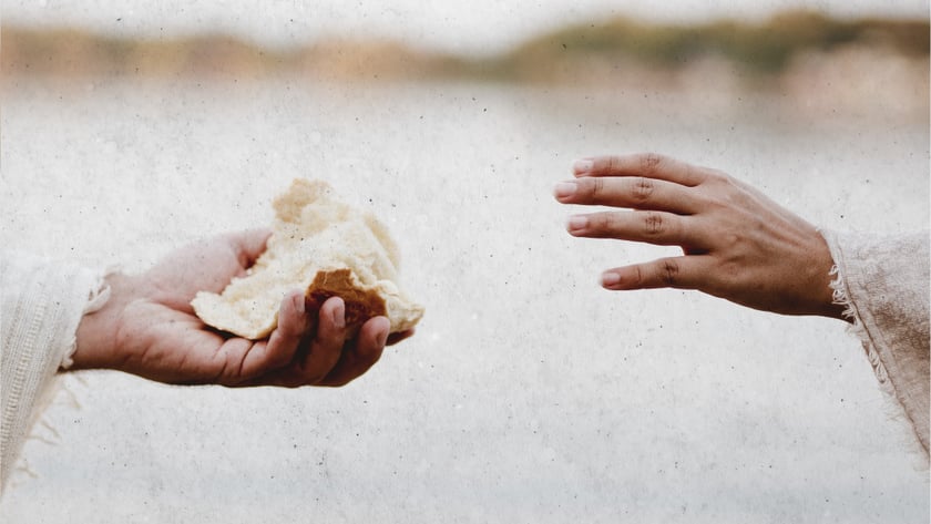 Uma mão segura um pedaço de pão e outra se estende para pegá-lo.