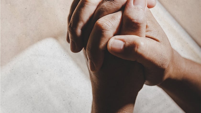 Mãos entrelaçadas em posição de oração sobre um livro aberto