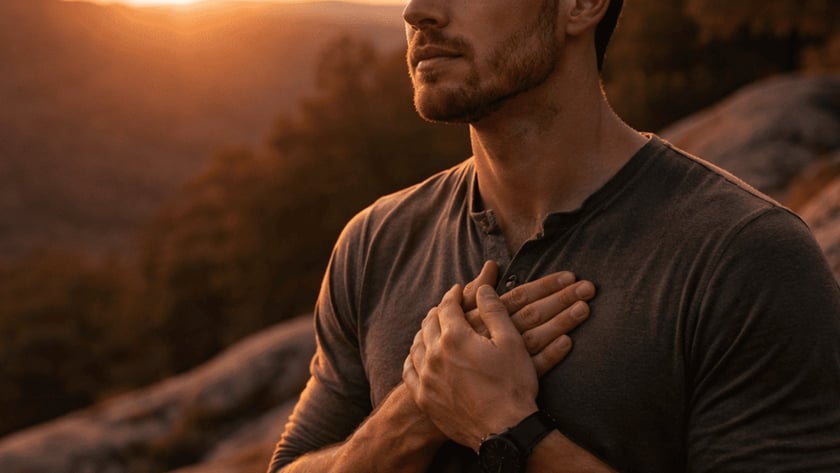 Homem de olhos fechados e mãos sobre o peito, em um mirante rochoso ao pôr do sol.