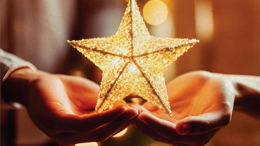 Duas mãos abertas seguram uma estrela dourada brilhante diante de luzes desfocadas.