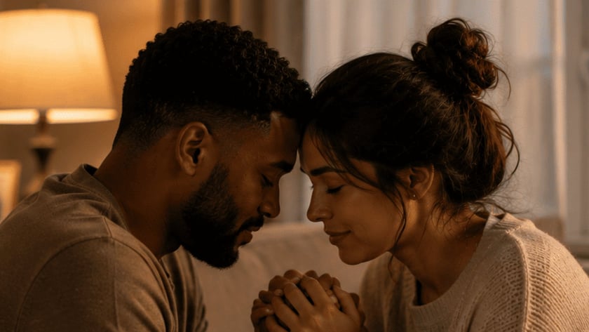 Casal sentado no sofá, com as testas encostadas e as mãos unidas, ao lado de uma Bíblia aberta.