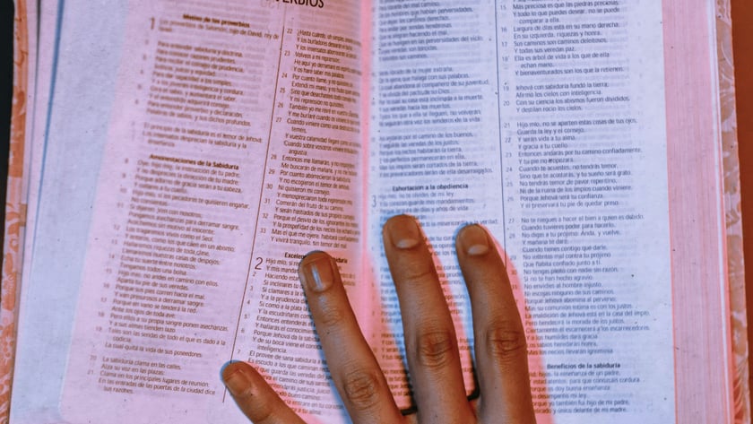 Mão espalmada sobre Bíblia aberta em espanhol, na página de "PROVERBIOS".