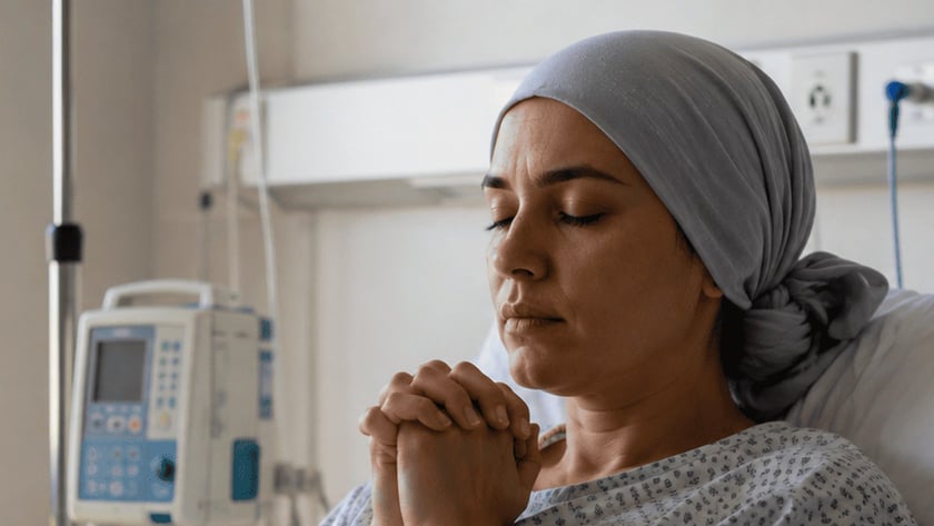 Mulher deitada em cama de hospital, de mãos juntas e olhos fechados, ao lado de soro.