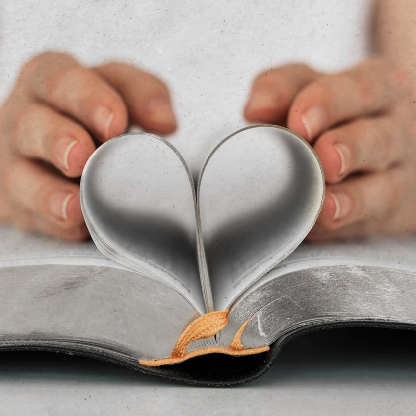 Duas mãos dobram as páginas de um livro aberto, formando um coração.
