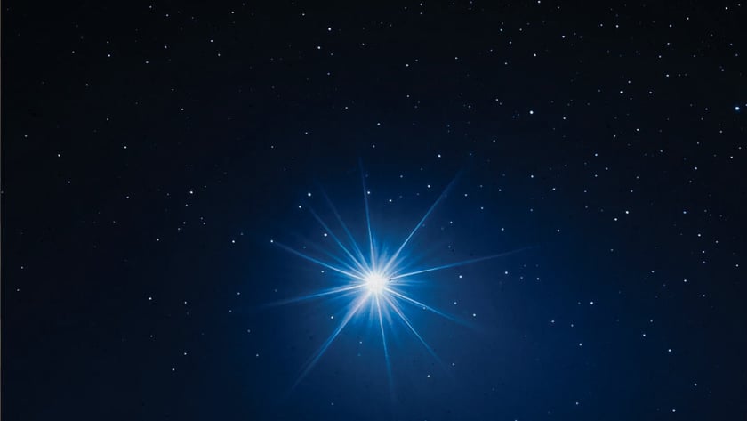 Estrela azul muito brilhante com raios longos, cercada por pequenas estrelas no céu escuro.