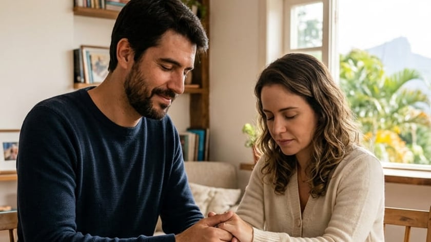 Homem e mulher de mãos dadas e olhos fechados sobre um livro aberto, à mesa.