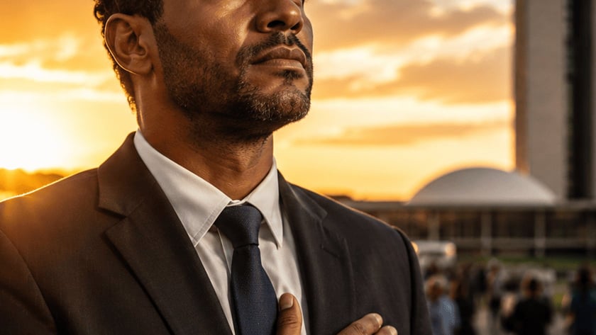 Homem de terno com a mão no peito olha para o alto, ao pôr do sol.