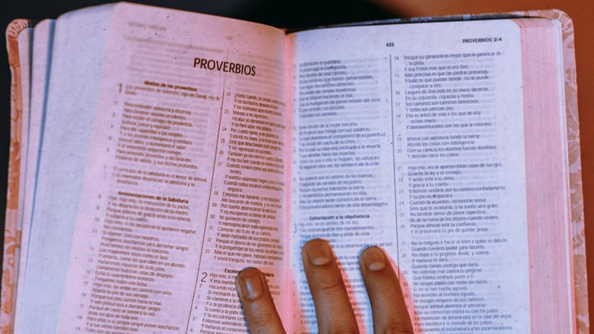 Mão espalmada sobre Bíblia aberta em espanhol, na página "PROVERBIOS".