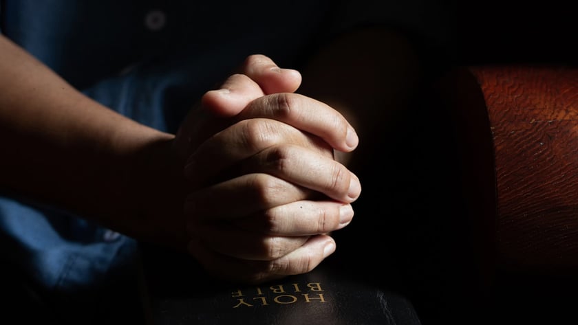 Mãos entrelaçadas sobre uma Bíblia preta fechada, com texto dourado "HOLY BIBLE".