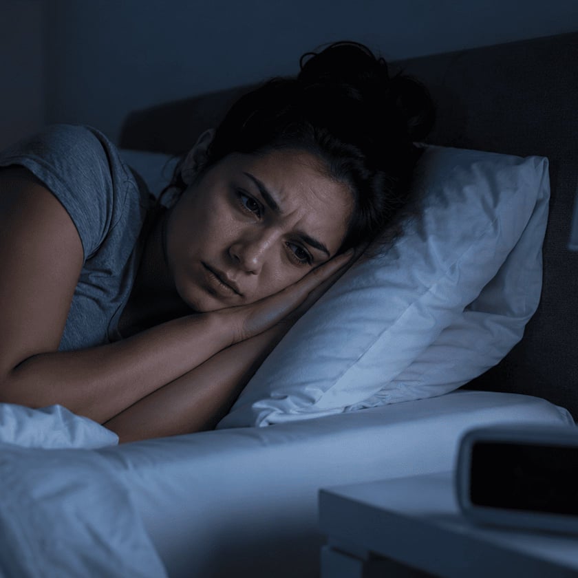 Mulher deitada na cama, de olhos abertos, olhando para o despertador na mesa de cabeceira.
