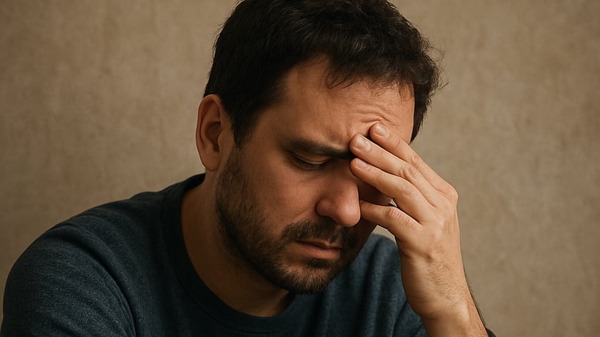 Homem de barba e suéter azul-escuro, de olhos fechados, com a mão na testa.