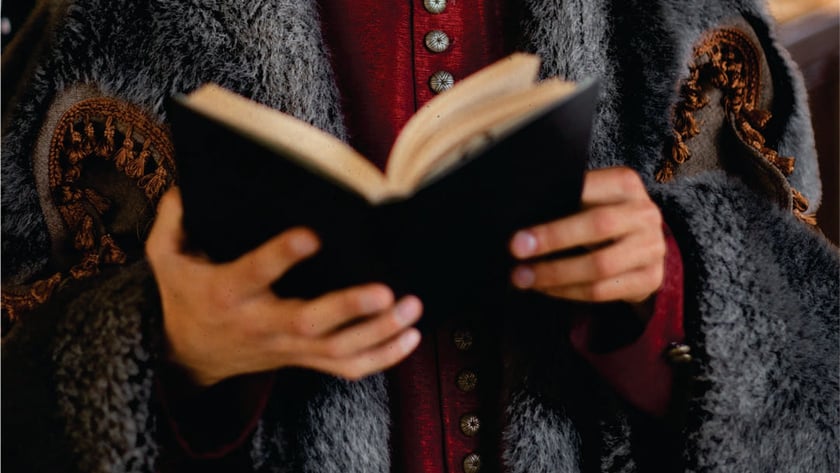 Pessoa com casaco vermelho e manto de pelo cinza lê um livro aberto.