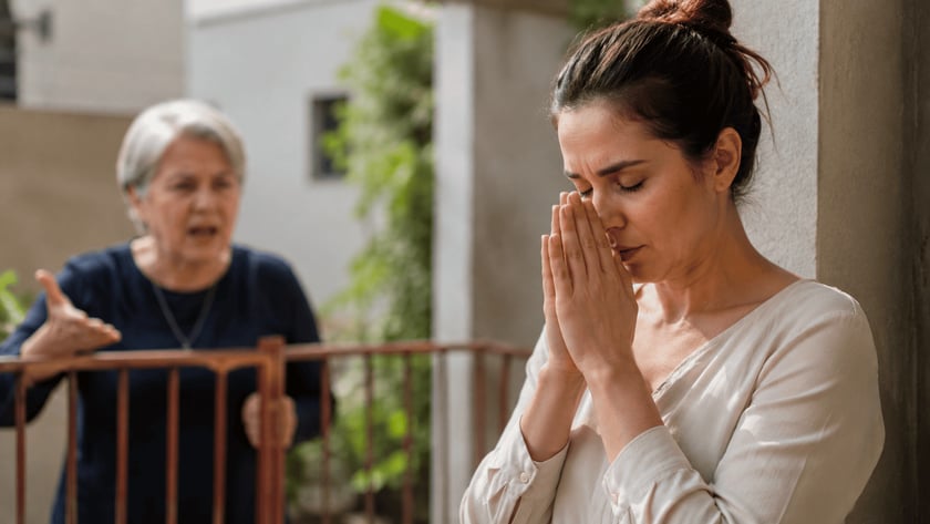 Mulher de olhos fechados e mãos unidas diante do rosto, em uma varanda.