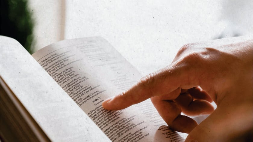 Mão apontando com o dedo indicador para um trecho de uma Bíblia aberta: "Psalm 72".