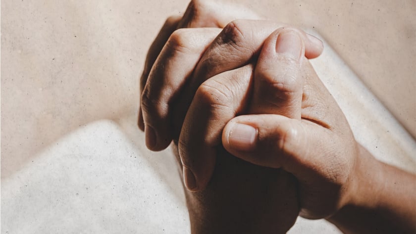 Mãos entrelaçadas em posição de oração sobre um livro aberto