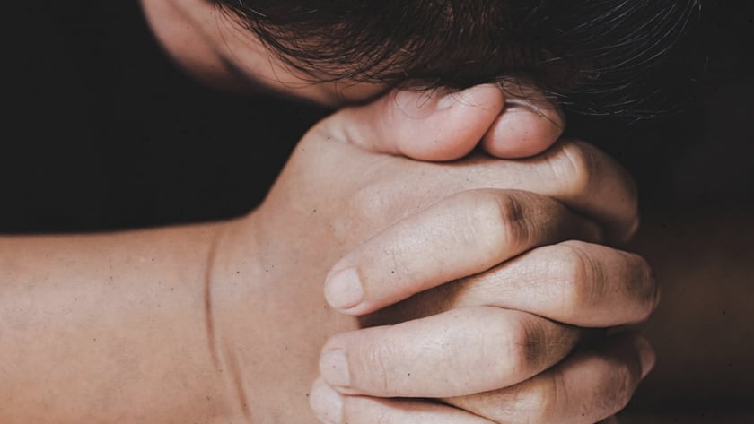 Pessoa de cabeça baixa, com as mãos entrelaçadas sobre uma Bíblia aberta.