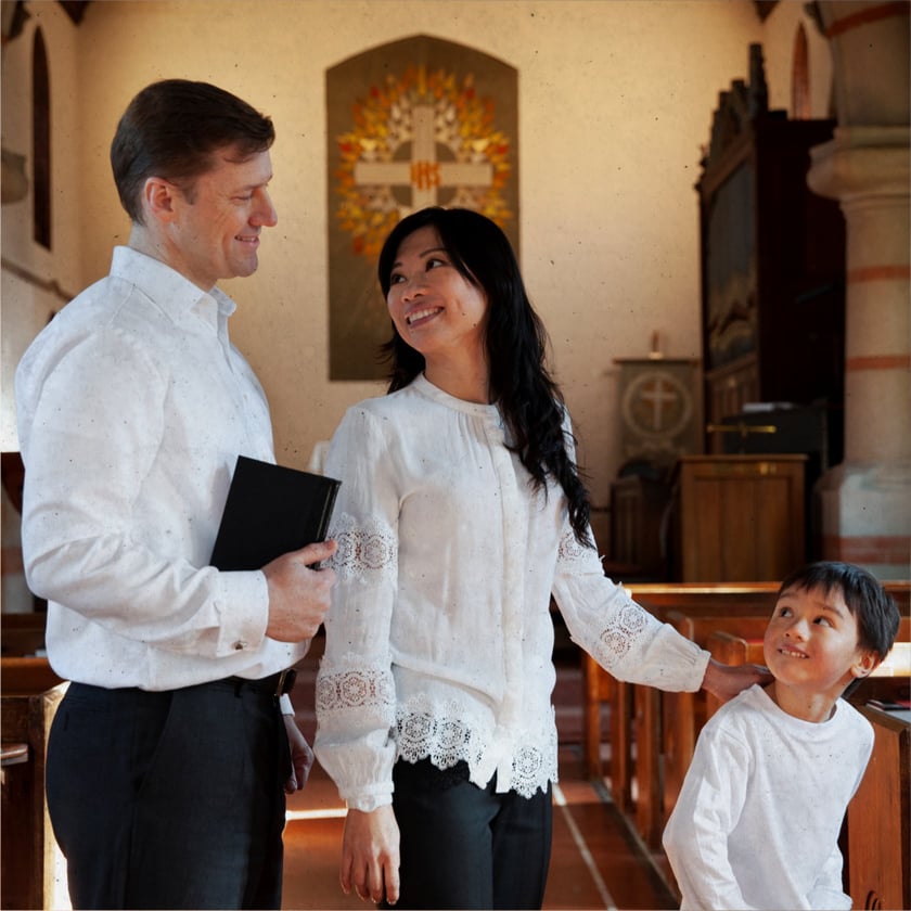 Homem, mulher e menino de roupas brancas sorriem entre si dentro de uma igreja.