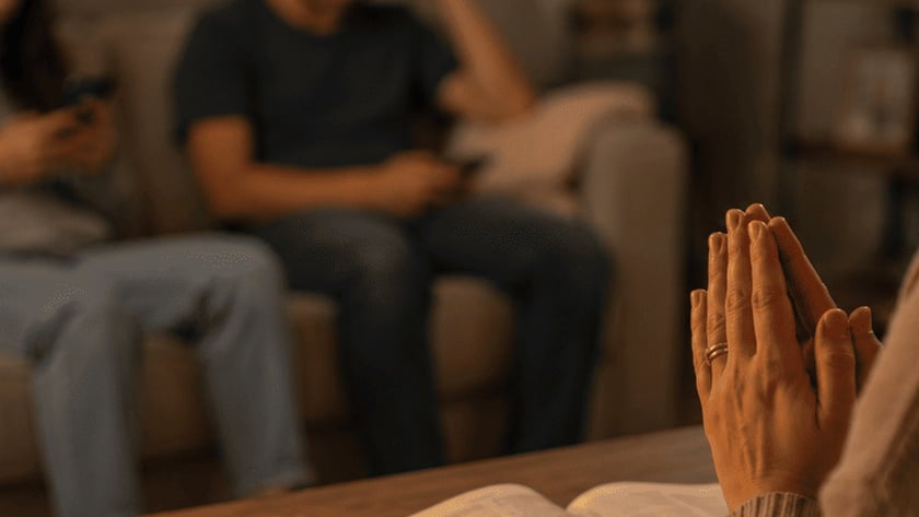 Dois jovens sentados num sofá usam celulares, com uma Bíblia aberta sobre a mesa à frente.