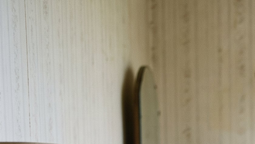 Mulher idosa de camisola sentada na beira da cama, olhando pela janela aberta.