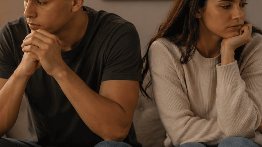 Homem e mulher sentados em um sofá, de costas um para o outro, com uma Bíblia aberta na mesa.