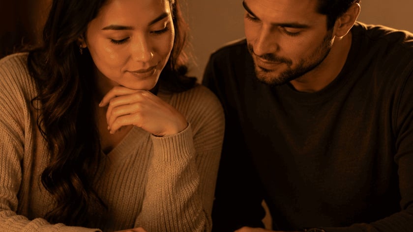 Casal lê junto uma Bíblia aberta sobre a mesa, perto de uma vela acesa.