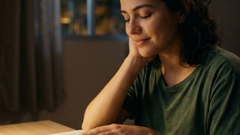 Mulher de olhos fechados, com a mão sobre um livro aberto, à mesa à noite.