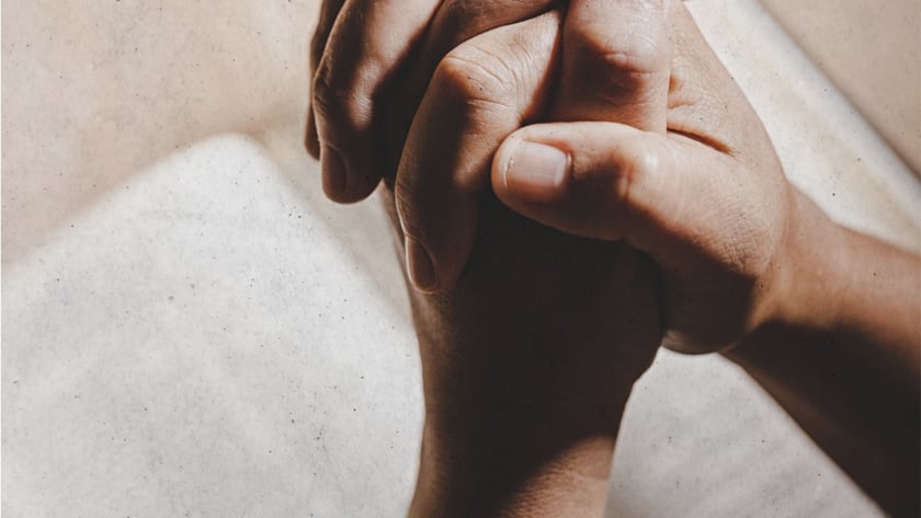 Mãos entrelaçadas em posição de oração sobre um livro aberto